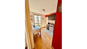 A modern kitchen with a red accent wall, a dining area with a table and chairs, and a view of the city through large windows. - LE TERRACOTTA T4 SLEEPS 6, AIR-CONDITIONED, WITH PARKING SPACE (Caluire-et-Cuire)
