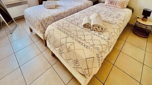 A room with two beds, a window with curtains, a wall-mounted artwork, and a small table with a lamp. - LE TERRACOTTA T4 SLEEPS 6, AIR-CONDITIONED, WITH PARKING SPACE (Caluire-et-Cuire)
