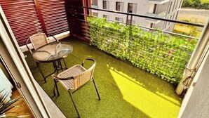 A balcony with artificial grass, a table with chairs, and a view of a modern building. - LE TERRACOTTA T4 SLEEPS 6, AIR-CONDITIONED, WITH PARKING SPACE (Caluire-et-Cuire)