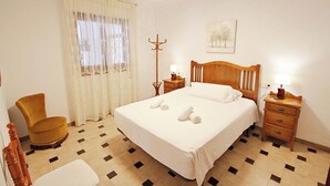 Een hotelkamer met een bed, een stoel, een nachtkastje, een lamp en een kapstok.