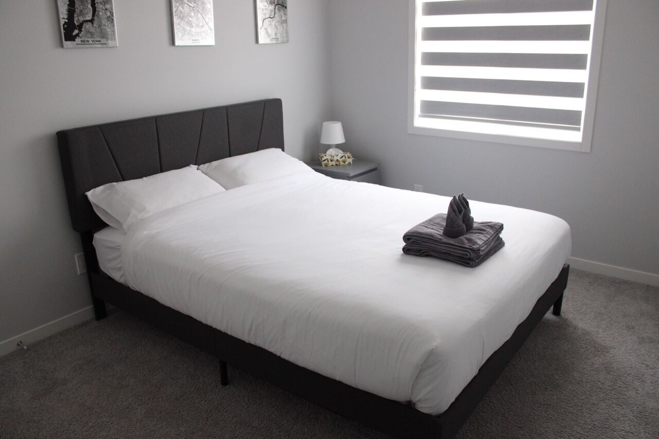 Een net opgemaakt bed met witte lakens, een donker hoofdbord en een gevouwen handdoek aan het voeteneinde.