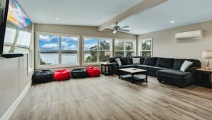 Amplia sala de estar con un ventanal grande, ventilador de techo y un sofá modular negro.