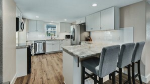Una cocina moderna con armarios blancos, lavavajillas integrado, refrigerador de acero inoxidable y encimera de mármol.