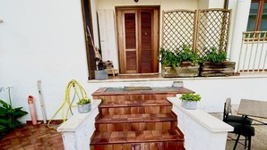 A set of outdoor steps leading to a door, surrounded by potted plants and a white wall.