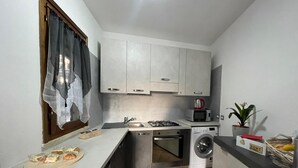 A compact kitchen with white cabinets, a gas stove, a microwave, a washing machine, and a small sink.