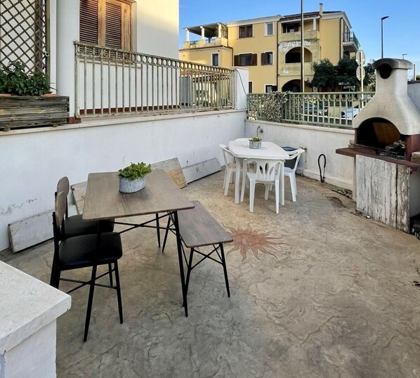 Eine Terrasse mit einem Holztisch, Stühlen, einem kleinen Topfpflanzen und einem Pizzaofen.
