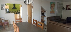 A dining area with a table and chairs, a living room with a sofa, and a kitchen in the background.