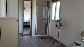A bedroom with a bed, a standing fan, a nightstand, and a wardrobe. - VILLA VAUNAGE (Calvisson)