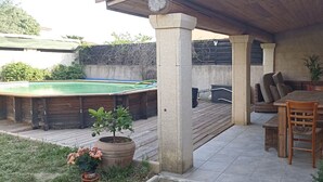 A covered patio area with a pool, wooden furniture, and potted plants. - VILLA VAUNAGE (Calvisson)