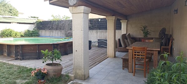 A covered patio area with a pool, wooden furniture, and potted plants.