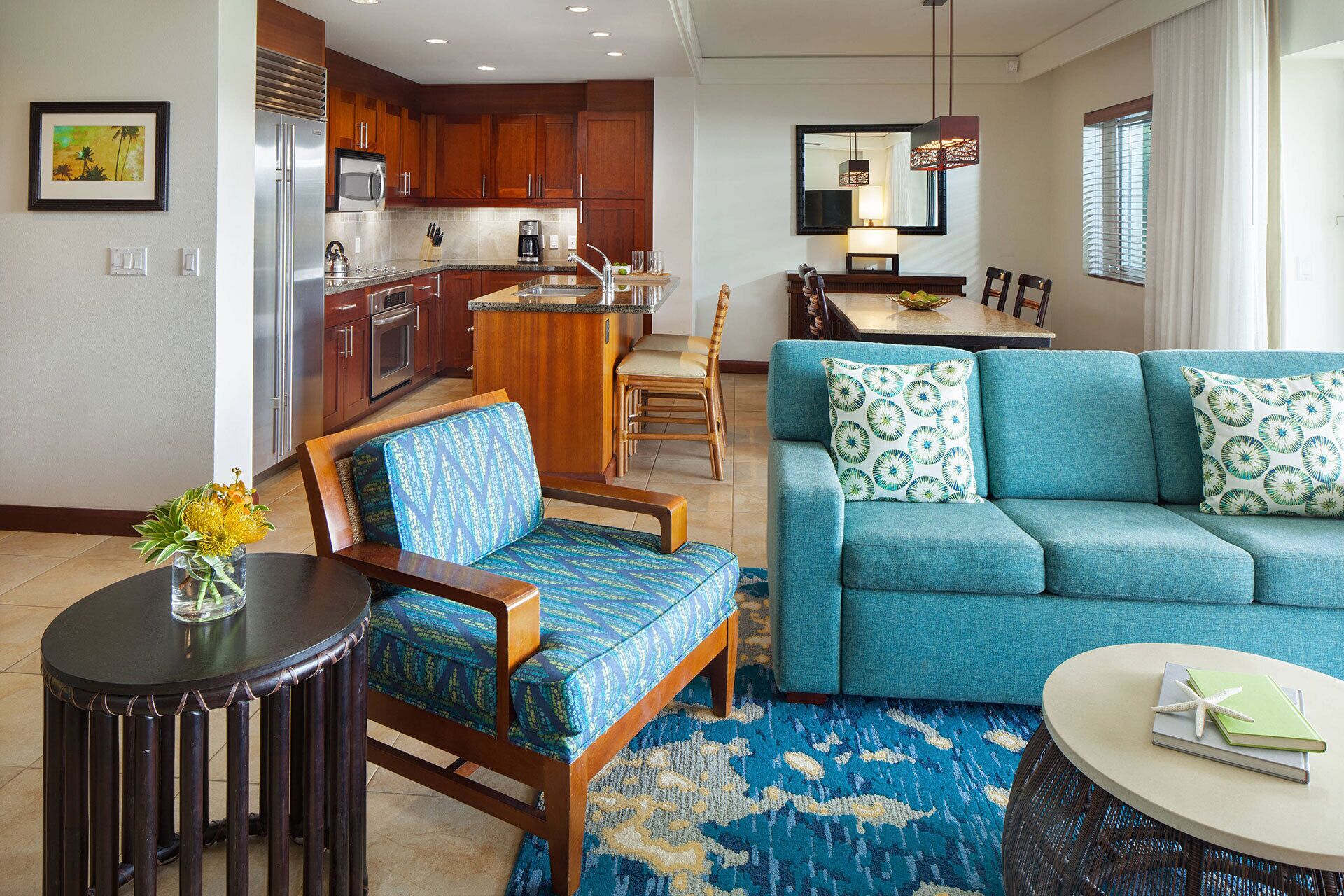 A modern living room with a blue sofa, a wooden chair, a round table, and a kitchen area in the background.