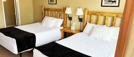 A hotel room with two beds, each with white linens and black bedspreads. There are two bedside tables with lamps, and the walls are painted a light beige color.