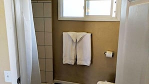 Ein Badezimmer mit Dusche, einem Handtuchhalter mit zwei Handtüchern und einem Fenster über dem Waschbecken.
