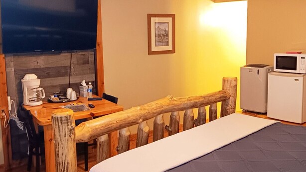 Ein gemütliches Zimmer mit einem hölzernen Bett, einem Schreibtisch mit Kaffeemaschine, einer Mikrowelle und einem gerahmten Bild an der Wand.