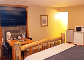 A cozy room with a wooden bed, a desk with a coffee maker, a microwave, and a framed picture on the wall. - Paiute Trails Inn (Marysvale)