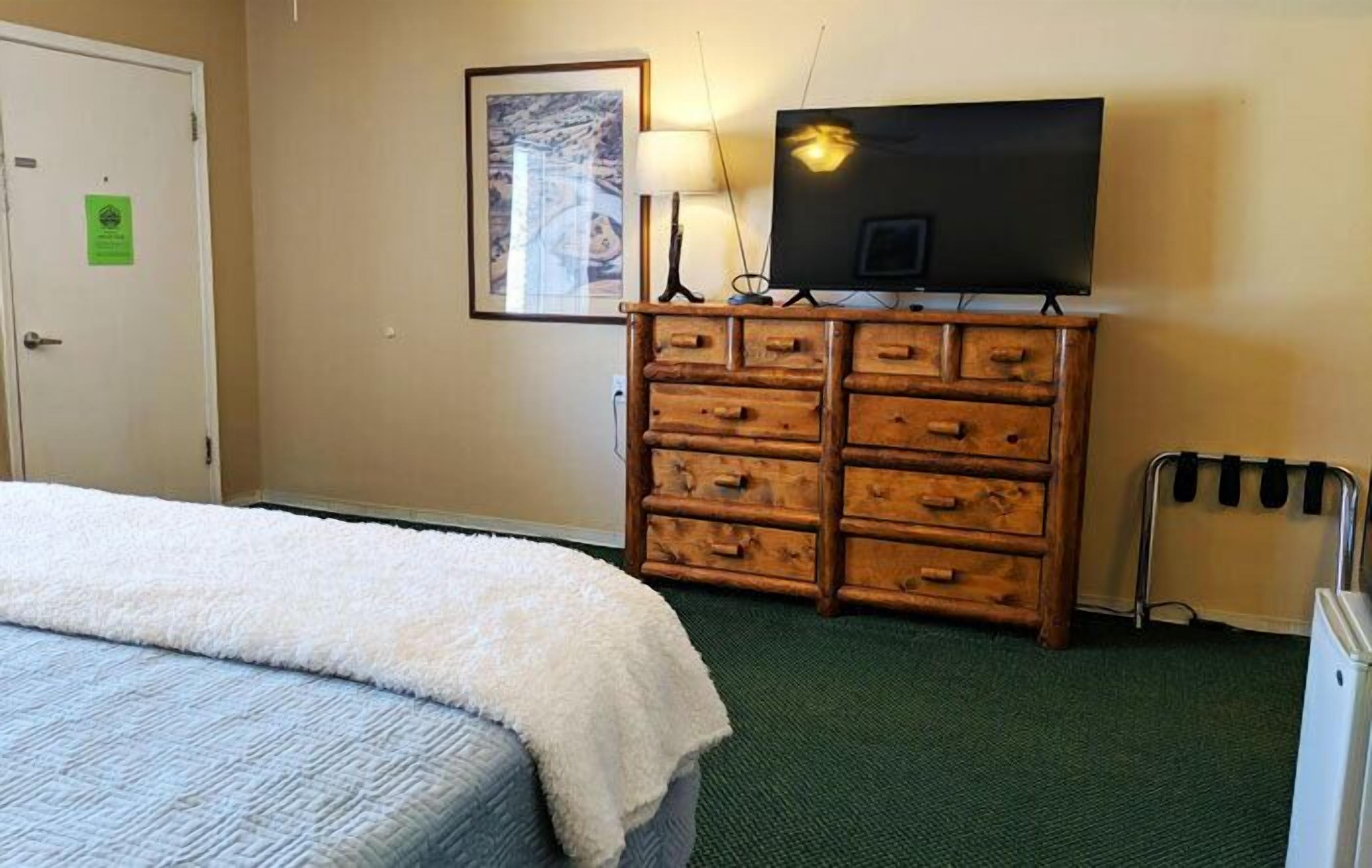 A hotel room with a bed, a wooden dresser, a television, and a radiator.