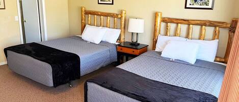 A hotel room with two beds, a door, a nightstand, and two framed pictures on the walls.