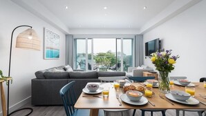 Ein modernes Wohnzimmer mit Essbereich, grauem Sofa und einem großen Fenster mit Blick auf die Stadt.