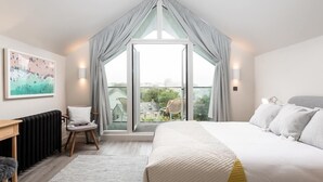 Ein Schlafzimmer mit großem Fenster, einem Bett, einem Schreibtisch und einem Sessel.