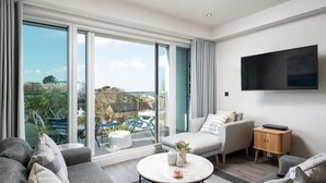 Ein modernes Wohnzimmer mit einem grauen Sofa, einem weißen Sessel, einem runden Couchtisch und einem an der Wand montierten Fernseher.