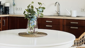 Een keuken met een witte tafel, een bloemenvaas en houten kastjes.