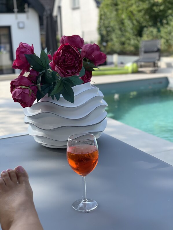 A glass of red wine on a table with a white vase of flowers.