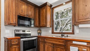 A kitchen with wooden cabinets, stainless steel appliances, and a window with a tree view.