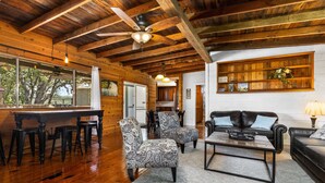 A spacious living area with wooden floors, a ceiling fan, a dining table with chairs, a sofa, and a coffee table.