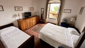 Ein Schlafzimmer mit zwei Betten, einem Holzschrank, einem Fernseher und einem Fenster mit Vorhängen.