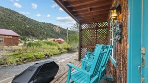 Une terrasse en bois avec des chaises turquoise, un barbecue et une vue sur une rivière et des montagnes.