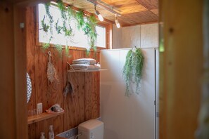 Un intérieur en bois comprenant des toilettes, des étagères avec des serviettes et des plantes suspendues.