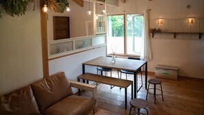 A cozy room with a wooden bench, a table, and a sofa. There are two stools and a cabinet with a shelf. - FamC (Nakafurano)