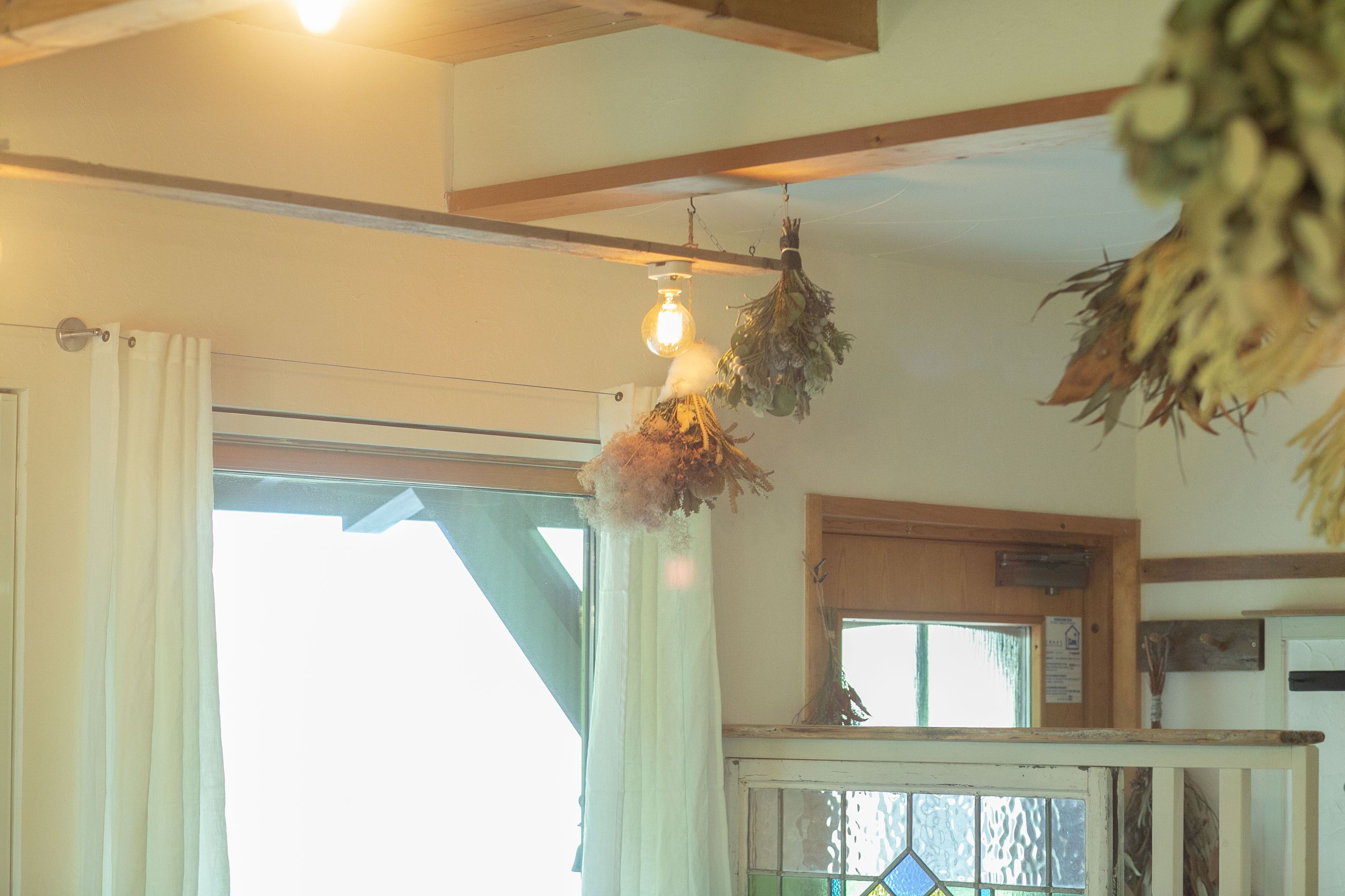 A room with a wooden ceiling, a hanging light fixture, a window with curtains, and a door.