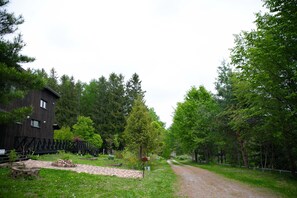 Un bâtiment rustique en bois, doté d’une zone pavée et d’un sentier de terre qui traverse une zone boisée.