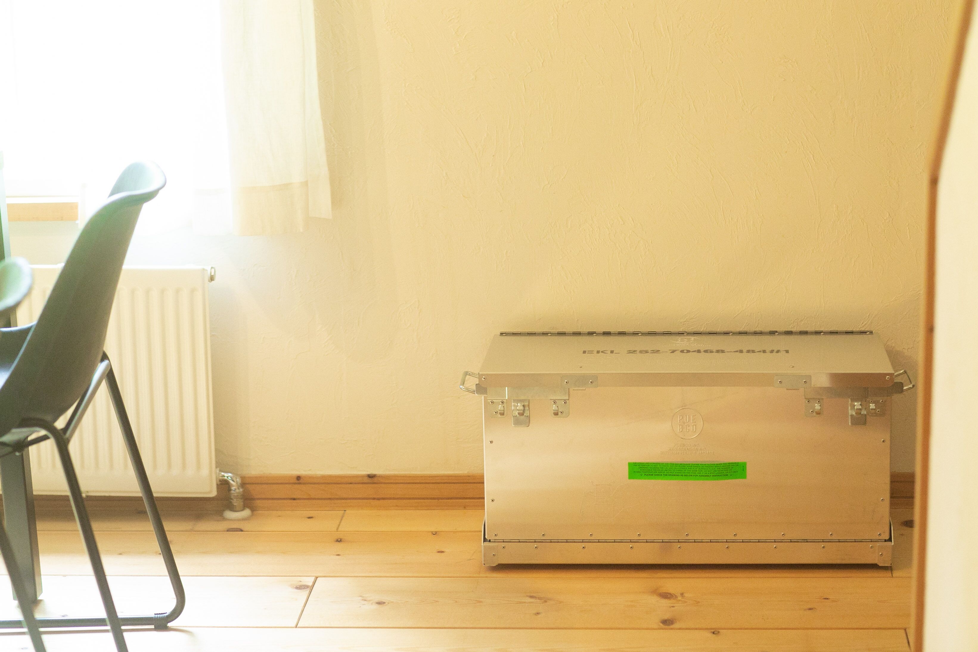 Una habitación con un radiador, una silla y un baúl metálico.