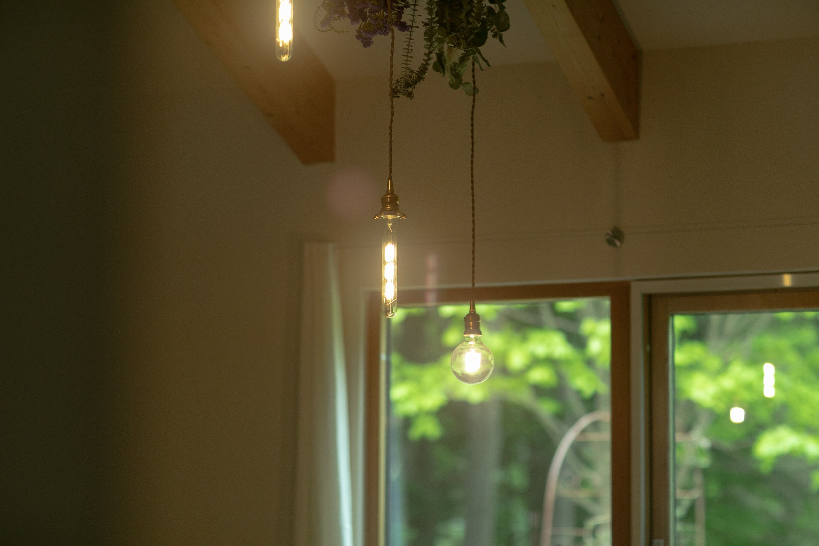 A room with a wooden ceiling, a hanging light fixture, and a window with a view of greenery outside.
