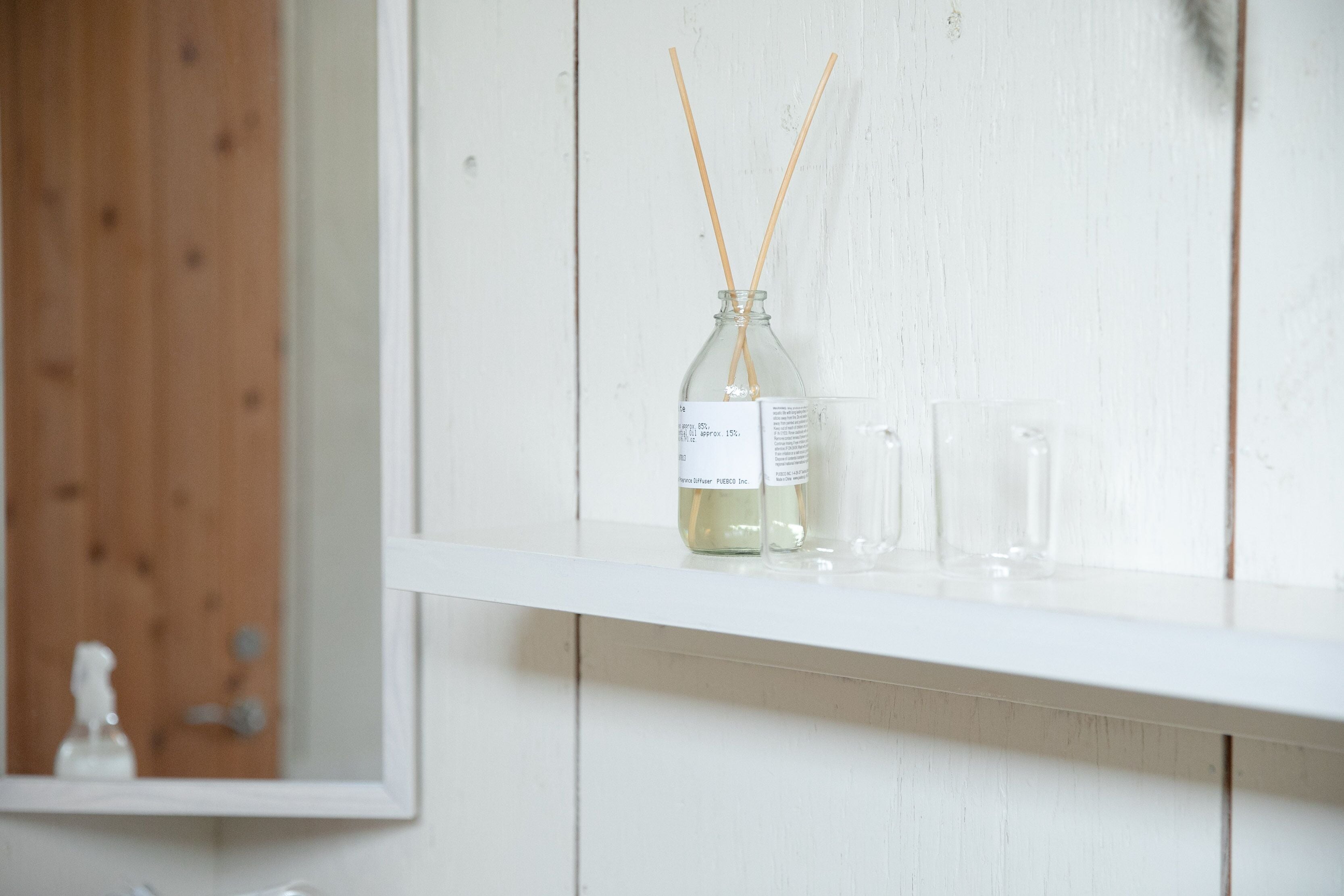 A white shelf with a glass bottle and two clear glasses.