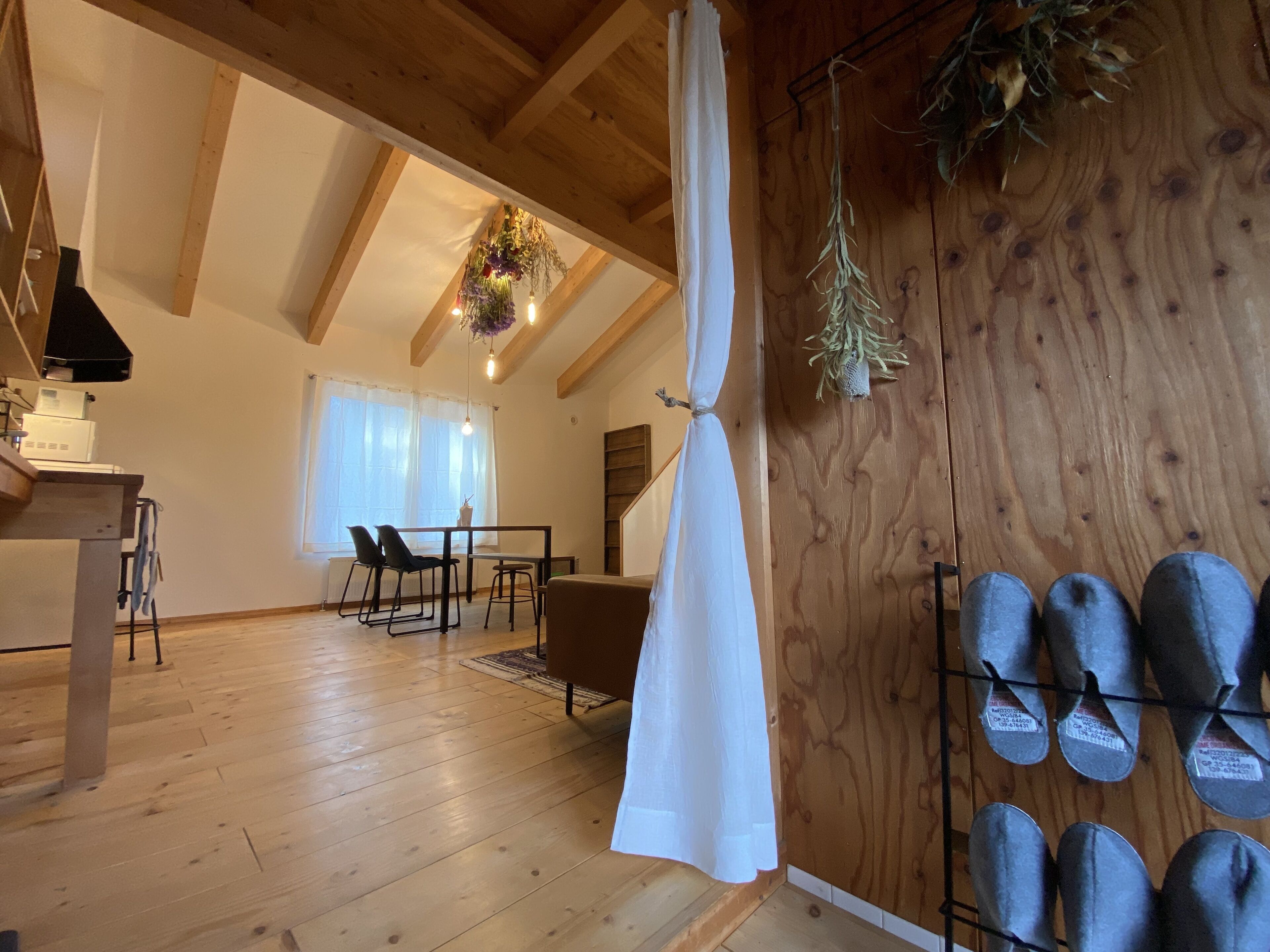 Um quarto espaçoso com vigas de madeira, uma área de jantar com cadeiras, uma planta pendurada e um sapateiro com sapatos.
