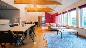 A spacious living area with a long wooden table, several chairs, a sofa, and a patterned rug. - THE FAM (Nakafurano)