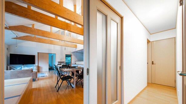A spacious room with a wooden floor, a dining area with chairs and a table, a TV, and a door leading to another room. - THE FAM (Nakafurano)