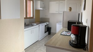 Une cuisine compacte avec des meubles blancs, un plan de travail, une machine à café et un lave-linge.