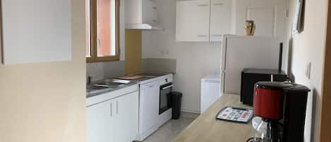 A compact kitchen with white cabinets, a countertop, a coffee maker, and a washing machine.