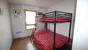 Une chambre avec un lit superposé, une échelle, une fenêtre et un tableau encadré au mur.