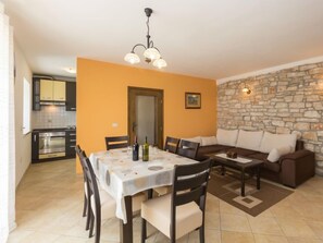 A dining area with a table set for four, a stone wall, and a kitchen in the background. - Vacation home Cvitan by Interhome (Tinjan)