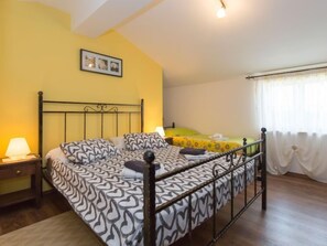 Un dormitorio con cama, mesita de noche, lámpara, ventana con cortinas y un cuadro en la pared.