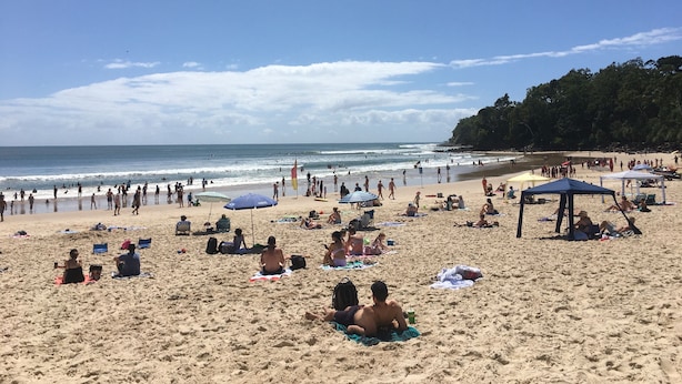 Una playa con gente tomando el sol, sombrillas y sillas de playa.