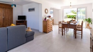 A modern living room with a sofa, TV, wooden cabinet, and a dining area with a table and chairs. - l'Emeraude by Interhome (Saint Cast le Guildo)