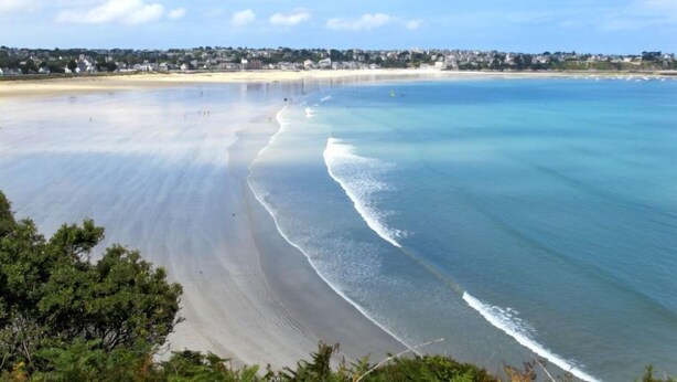 A beach with clear water, a sandy shore, and a distant residential area. - l'Emeraude by Interhome (Saint Cast le Guildo)
