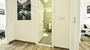 Ett modernt hotellrum med trägolv, en tavla som föreställer ett bergslandskap, ett badrum med en vägg täckt av gröna kakelplattor och en vit säng.