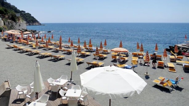 A beachside area with rows of sun loungers and umbrellas, a wooden deck with tables and chairs, and a view of the sea. - Lambrusca by Interhome (Moneglia)
